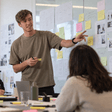 Facilitator pointing at a wall of sketches and sticky notes during a workshop
